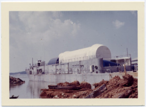 A Saturn rocket stage is loaded onto a barge on the Tennessee River.