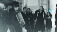 Photograph of multiple people standing in a room while a man in a hat plays the accordion at the 300th General Hospital in Naples, Italy.