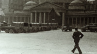 Photograph of army vehicles parked outside of a stone building in Italy.