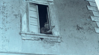 Photograph of a man waving from a windowsill.