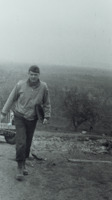 Photograph of a soldier with a clipboard walking uphill from a military vehicle.